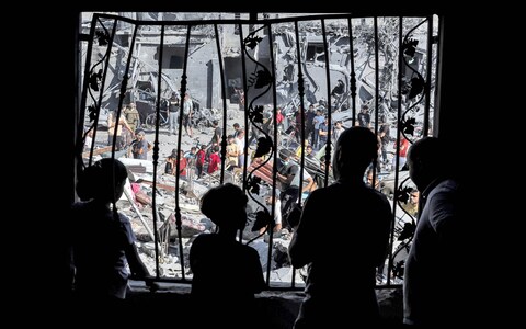 People stand behind the metal mesh that covered the window of a building that was hit by Israeli bombardment in Rafah in the southern Gaza Strip 