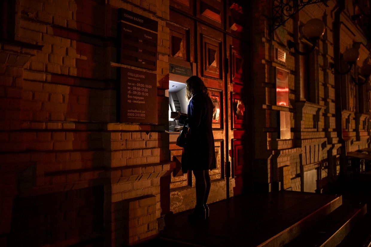 A woman operates a cash machine lit by a traffic light in Kyiv, Ukraine on Nov.8, 2022.